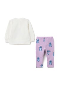 Witte lange mouwen top met knopen op de rug, gecombineerd met paarse leggings met een herhaald patroon van cartoonfiguren in blauw en roze.
