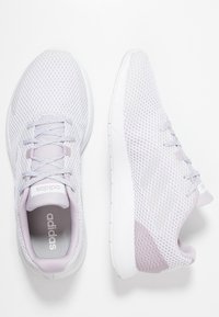 Chaussures de sport gris clair avec tige en mesh, bout rond, lacets fins et accents lilas doux ; design épuré avec surfaces texturées.