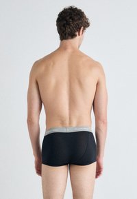 Črne bombažne bokserice z teksturiranim pasom, na katerem je siva oznaka Calvin Klein, prikazane zadaj.