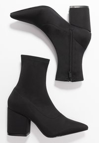 Bottines noires en tissu extensible, dotées d'un bout pointu, d'un talon carré et d'une fermeture éclair sur le côté. Texture lisse avec des coutures minimales.