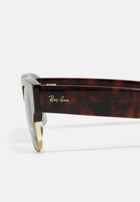 Ray-Ban prillid, millel on kilpkonnamuster, mustad raami, gradient objektiivid, kuldsed aksendid ja logo detailid templis.