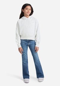 Svetlosivá skrátená mikina s klokankou a rebrovaným lemom, skombinovaná s modrými rifľami s rozšírenými nohavicami a bielymi teniskami.