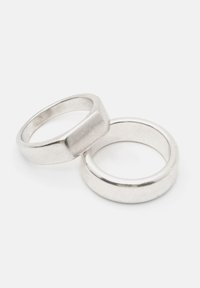 Två silverringar: den ena har en slät, rundad band, medan den andra har en platt yta med en något bredare design.