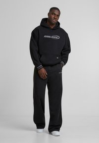 Black hooded sweatshirt and matching sweatpants. Smooth texture, relaxed fit, with ribbed accents and logo detail on the chest and pants.