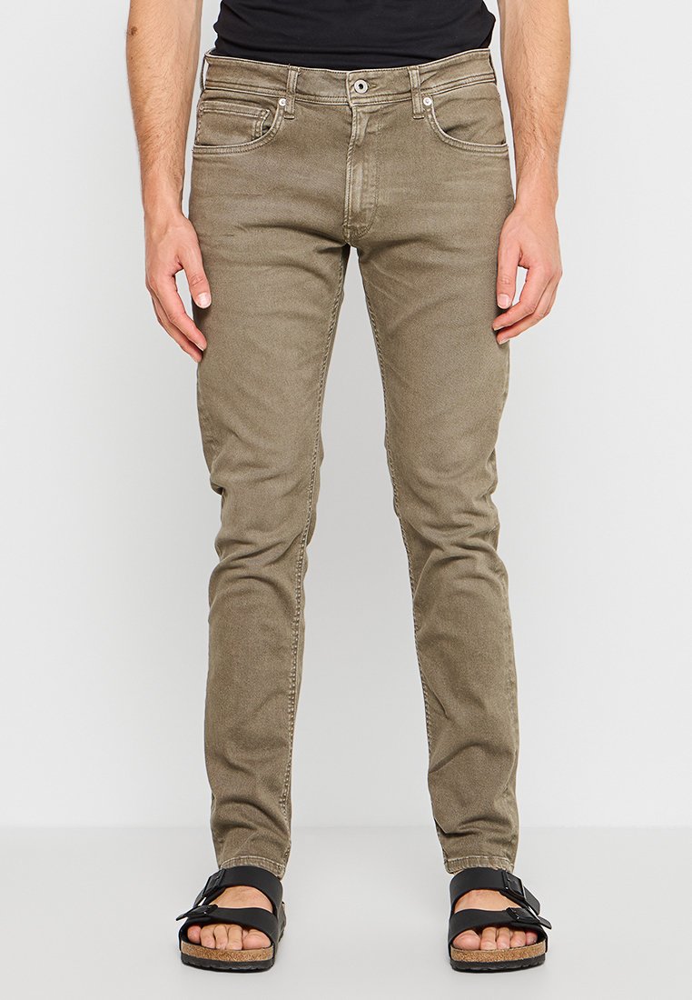 Jeans ajustados de color verde oliva con una textura suave, diseño de cinco bolsillos, cierre de botón y un ligero desgastado, combinados con sandalias negras.