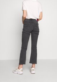 Grå utsvängda jeans med hög midja, rå kant och dekorativ sömnad; kombinerat med en enkel vit T-shirt och vita sneakers.