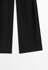 Zwarte wijde broek met rechte boorden, getoond van halverwege de dij tot aan de enkel op een witte achtergrond.