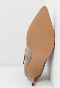 Brązowy zamszowy but na wysokim obcasie z szpiczastym noskiem, smukłym obcasem i teksturowaną beżową podeszwą; rozmiar oznaczony na spodzie jako 37.
