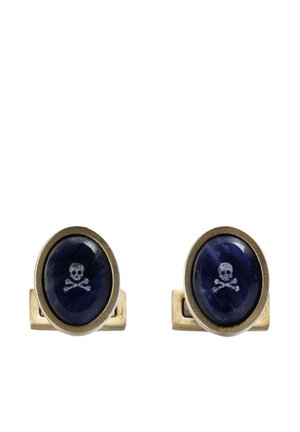 Par de gemelos ovalados de oro con piedras azul oscuro que presentan pequeños diseños de calavera y huesos cruzados en el centro.