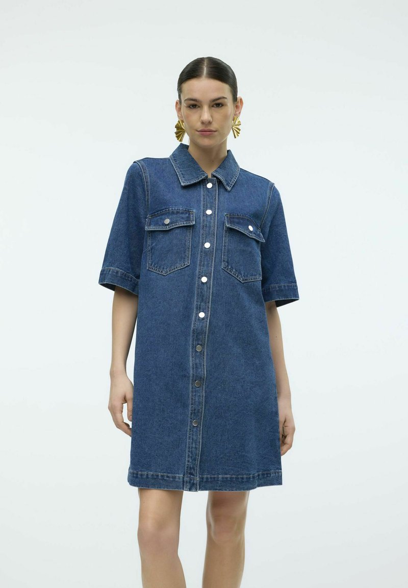 Denim skjortekjole med korte ermer, krage, to frontlommer og knappeåpning foran. Mørk blå farge med en teksturert overflate.