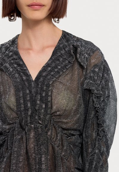 Blouse noire transparente avec une finition métallique texturée. Présente des accents volants et un décolleté plongeant, mettant en valeur un tissu doux et fluide.
