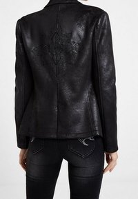 Veste en faux cuir noir avec une silhouette ajustée, présentant un embossage floral dans le dos, une texture lisse et un col ajusté.