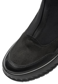 Zapatilla deportiva negra que presenta una combinación de parte superior de ante y textil, con una puntera de cuero liso y suela de goma texturizada.