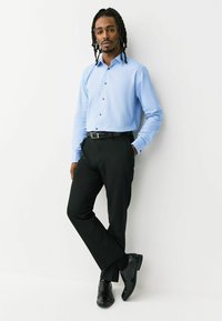 Svetlomodrá košeľa na zapínanie s textúrovaným vzorom, kombinovaná s čiernymi nohavicami a lesklými čiernymi topánkami. Oblečenie dopĺňa čierny opasok.