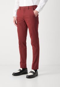 Czerwone, dopasowane spodnie o gładkiej fakturze, z płaskim przodem, bocznymi kieszeniami i smukłym krojem. Połączone z czarnymi mokasynami z białymi akcentami.
