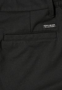 Tissu noir avec une poche arrière et une petite étiquette portant l'inscription "Street One Men Unmatched Comfort" près de la taille.