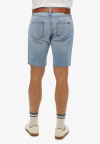 Pantalones cortos de denim azul claro con un corte clásico, que cuentan con cinco bolsillos y un dobladillo deshilachado. Llevados con un cinturón marrón, zapatos crema y calcetines a rayas.