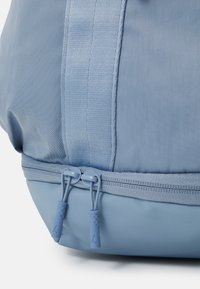 Plavi tkaninski ruksak s glatkom teksturom, sa pojačanim dnom, kontrastnim bočnim šavovima i dva rajsferšlusa s teksturiranim hvataljkama.