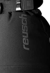 Sort polstret stof med et prægede "reusch" logo. Har en grå rem med en metalspænde. Viser en glat tekstur og syede detaljer.