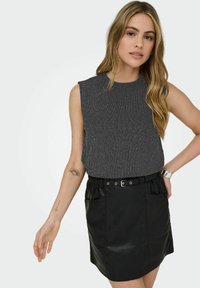 Czarna mini spódnica z eko skóry z dwoma kieszeniami, zestawiona z ciemnym, bezrękawnym topem o żebrowanej fakturze. Posiada taliowany pas z srebrną klamrą.