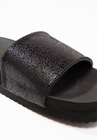 Black slide sandal featuring a textured, cracked leather upper and a matte black footbed with a slightly raised sole for grip.
