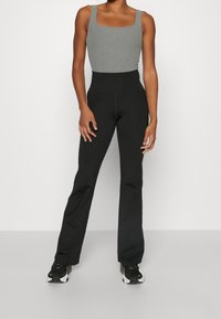 Szary bodysuit z kwadratowym dekoltem w połączeniu z czarnymi spodniami z wysokim stanem i szerokimi nogawkami. Materiał wydaje się gładki z elastyczną fakturą. Całość uzupełniają czarne sneakersy.