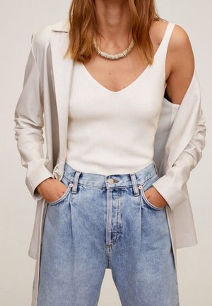 Valkoinen ribbineulottu hihaton paita vaalean beigen bleiserin alla; vaaleansiniset, korkeavyötäröiset farkut, joissa on rento istuvuus ja hienovaraiset etukulmut.