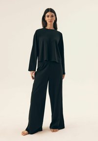 Czarny longsleeve z luźnym krojem i okrągłym dekoltem, w połączeniu z szerokimi czarnymi spodniami, wykonanymi z miękkiej, gładkiej tkaniny.