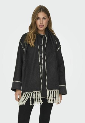Cappotto di lana nera con vestibilità ampia, cuciture decorative bianche e orlo frangiato, dotato di grandi bottoni e maniche lunghe.