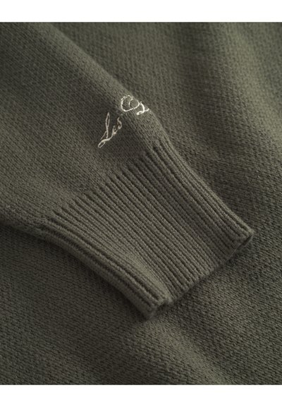 Pull en tricot vert foncé avec une surface texturée. Doté de poignets côtelés et d'un petit logo brodé près de la manche.