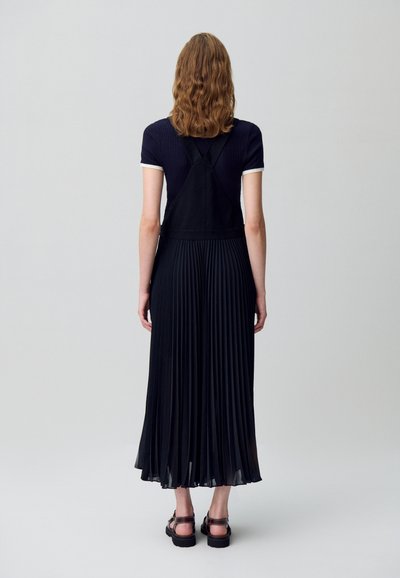 Robe noire plissée avec un haut ajusté et des bretelles larges. Présente une texture côtelée sur le corsage, un tissu fluide et un drapé doux.