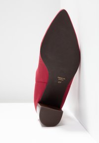 Chaussure femme rouge à bout pointu avec semelle noire, talon bloc, taille 37, fabriquée en Espagne, vue du dessous sur fond blanc.