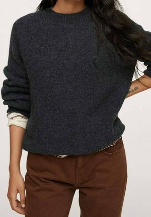 Mørkegrå strikket sweater med rund halsudskæring, afslappet pasform og ribbede ærmegab, båret over en lysefarvet langærmet skjorte, kombineret med brune bukser.