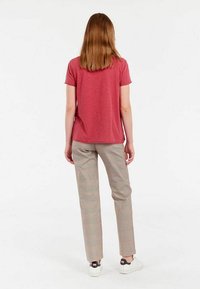 T-shirt rouge à manches courtes associé à un pantalon à carreaux légers, avec une coupe décontractée et des baskets blanches avec des accents noirs.