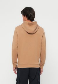 Felpa con cappuccio marrone, dal tessuto morbido, con polsini e orlo a costine. Presenta una tasca a marsupio e nessun logo o design visibile.