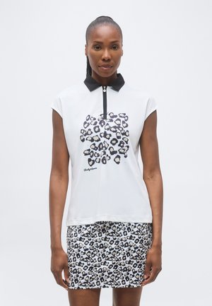 Vrouw draagt een witte mouwloze polo met een zwarte kraag en een luipaardprint, gecombineerd met een bijpassende luipaardprint rok.