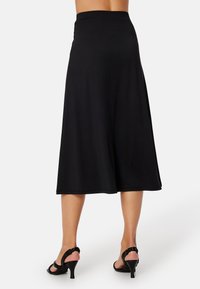 Mustaan, polvenpituinen A-linjainen hame joustavalla vyötäröllä. Valmistettu pehmeästä kankaasta, jossa on sileä rakenne. Yhdistetty mustiin korkokenkiin.