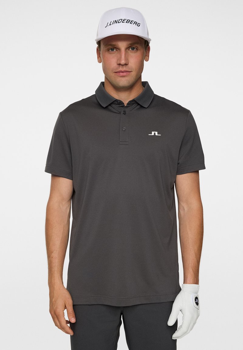 Grå pikétröja med krage och korta ärmar, med en vit logotyp på bröstet. Bärs med en vit keps och vita golfhandskar.