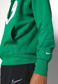 Sweat à capuche vert avec un grand graphique blanc et une poche kangourou à l'avant. Comprend des poignets côtelés et un petit logo Nike blanc.