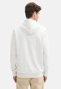 Sudadera gris claro con capucha, textura suave, puños y dobladillo acanalados, y un diseño limpio. Detalle de costura visible en la parte posterior.