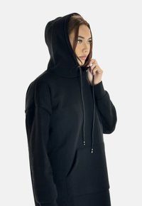 Sudadera con capucha negra y bolsillo tipo canguro, fabricada en tejido suave. Cuenta con cordones ajustables y un diseño de corte relajado.