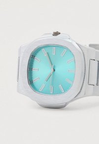 Ασημένιο μεταλλικό ρολόι χειρός με τετράγωνη θήκη και τυρκουάζ καντράν που δείχνει την ώρα 6:56, με ασημένιους δείκτες και δείκτες ώρας.