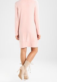 Abito lungo a maniche lunghe di colore rosa chiaro, con taglio dritto, texture morbida e orlo fino al ginocchio. Abbinato a stivali alla caviglia beige con tacco.