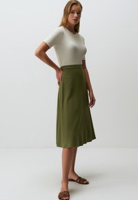 Jupe A-line vert clair en tissu doux avec une texture lisse. Assortie à un haut blanc ajusté à côtes et des sandales marron.