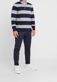Randig långärmad polo i marinblå och grå, med en ljusblå krage, matchad med marinblå byxor och vita sneakers. Har en bröstlogotyp.