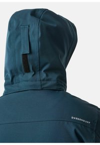 Blå huva jacka med slät textur, med en Velcro-flik och vit "SWEDEMOUNT" logotyp på axeln. Bakvyn visar sömdetaljer.