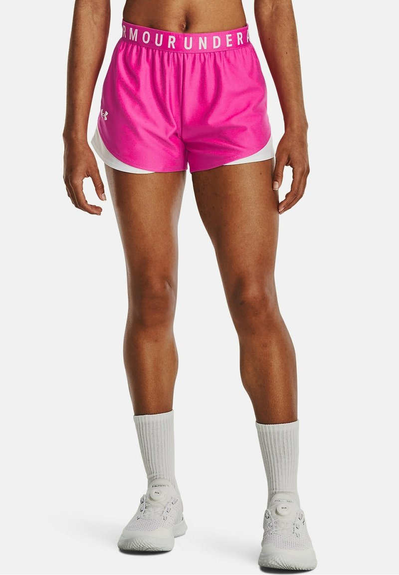 Rosa idrottsshorts med vita sidodetaljer, elastisk midja med texten "ARMOUR UNDER". Bärs med vita ankelsockor och träningsskor.