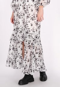Weißes Kleid mit schwarzem Blumenmuster, geschichtete Rüsche am Saum und seitlichem Schlitz, kombiniert mit klobigen schwarzen Knöchelstiefeln. Leichter Stoff.