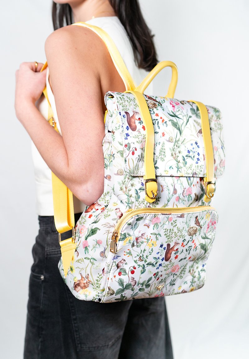 Zaino con motivo floreale, con spallacci gialli e accessori in oro. Forma rettangolare con tasca frontale con zip e spallacci regolabili.