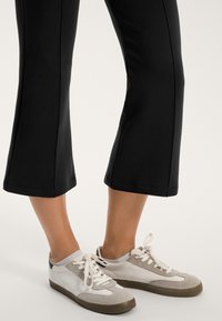 Baskets blanches et grises avec des lacets, en matériaux en daim et en cuir lisse. Pantalons noirs coupés avec un design droit et un ourlet.